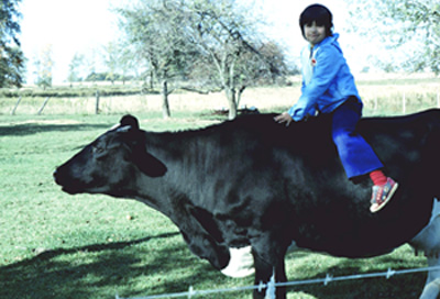 Me as a little goober riding Lilah the cow in the pasture. If you look real closely, you'll notice she's considering walking under a low branch to knock me off.